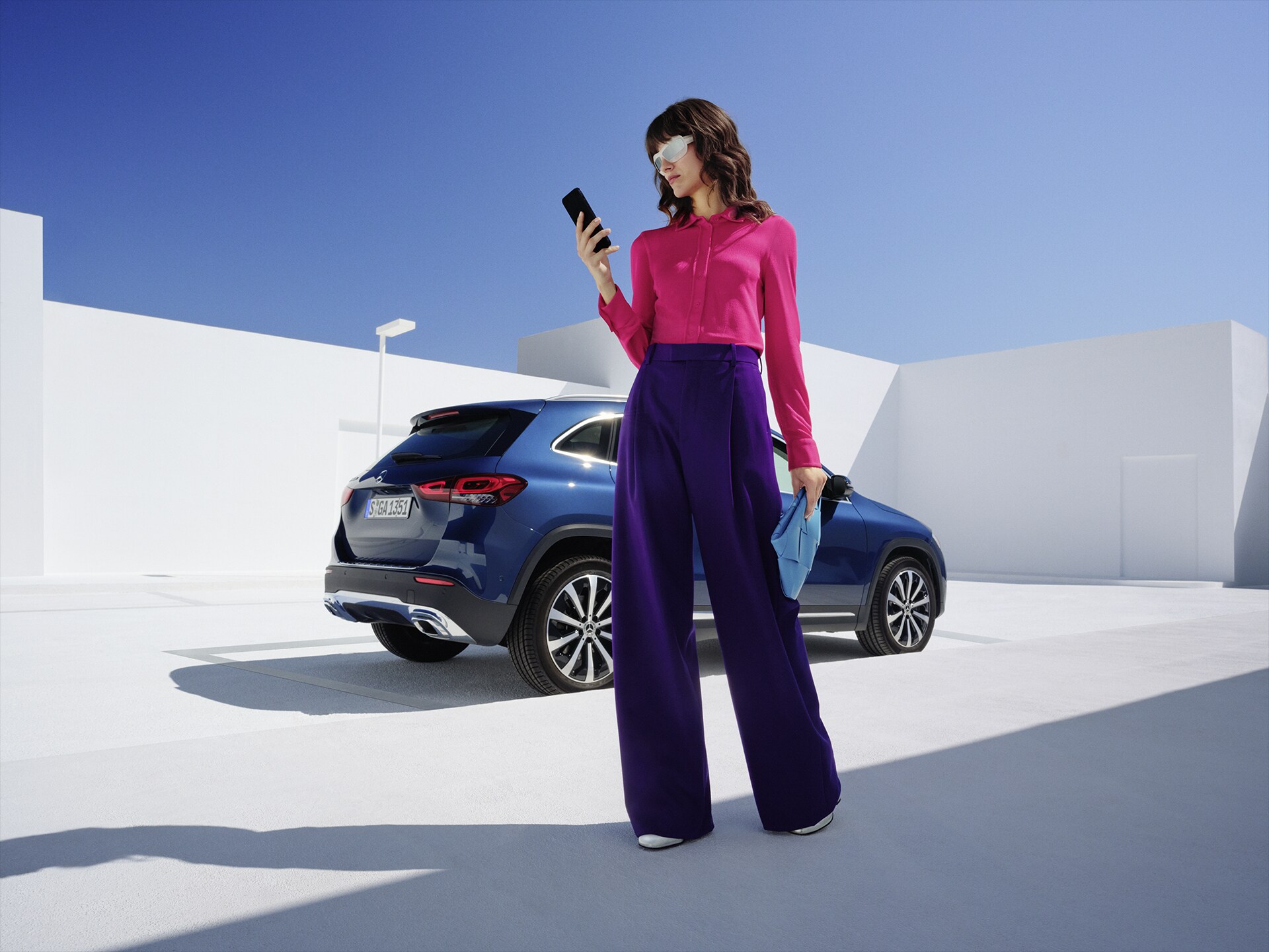 Eine Frau steht vor dem Mercedes-Benz GLA und schaut auf ihr Telefon.