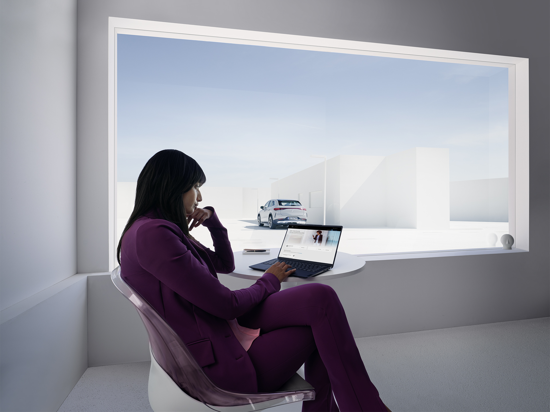 Geschäftsprofil-Vorteile | Mercedes me ID | Mercedes-Benz Eine Frau, die an einem Laptop arbeitet, sitzt in einem weißen Büro vor einem großen Fenster.