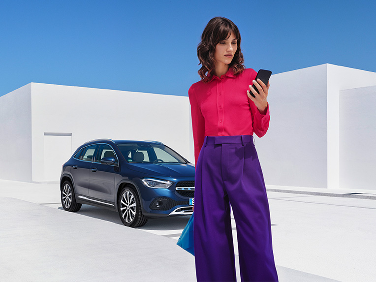 Eine Frau stellt per Mercedes me App auf ihrem Smartphone eine Verbindung mit ihrem Mercedes-Benz her. Eine Frau stellt per Mercedes me App auf ihrem Smartphone eine Verbindung mit ihrem Mercedes-Benz her.