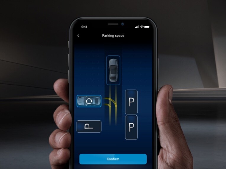 Mit einem Smartphone wird ein Mercedes-Benz per Mercedes me App Remote Parkdienst eingeparkt. 