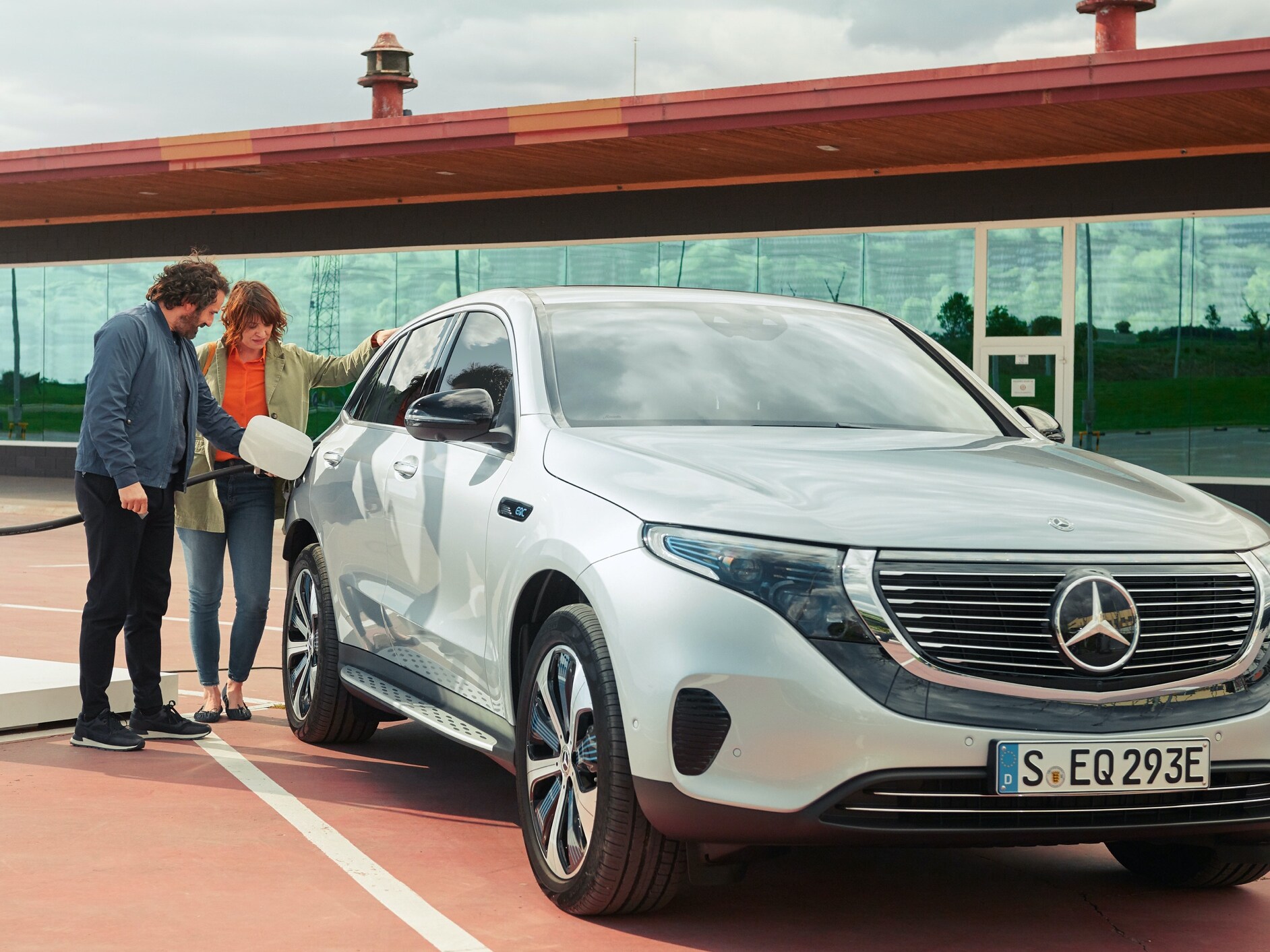 Ein Mann und eine Frau laden ihren Mercedes-Benz bequem an einer Ladesäule per Digitalen Extras zum Thema Charge.