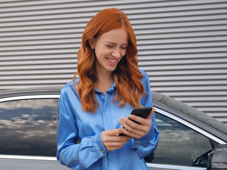 Eine Frau stellt per Mercedes me App auf ihrem Smartphone eine Verbindung mit ihrem Mercedes-Benz her.