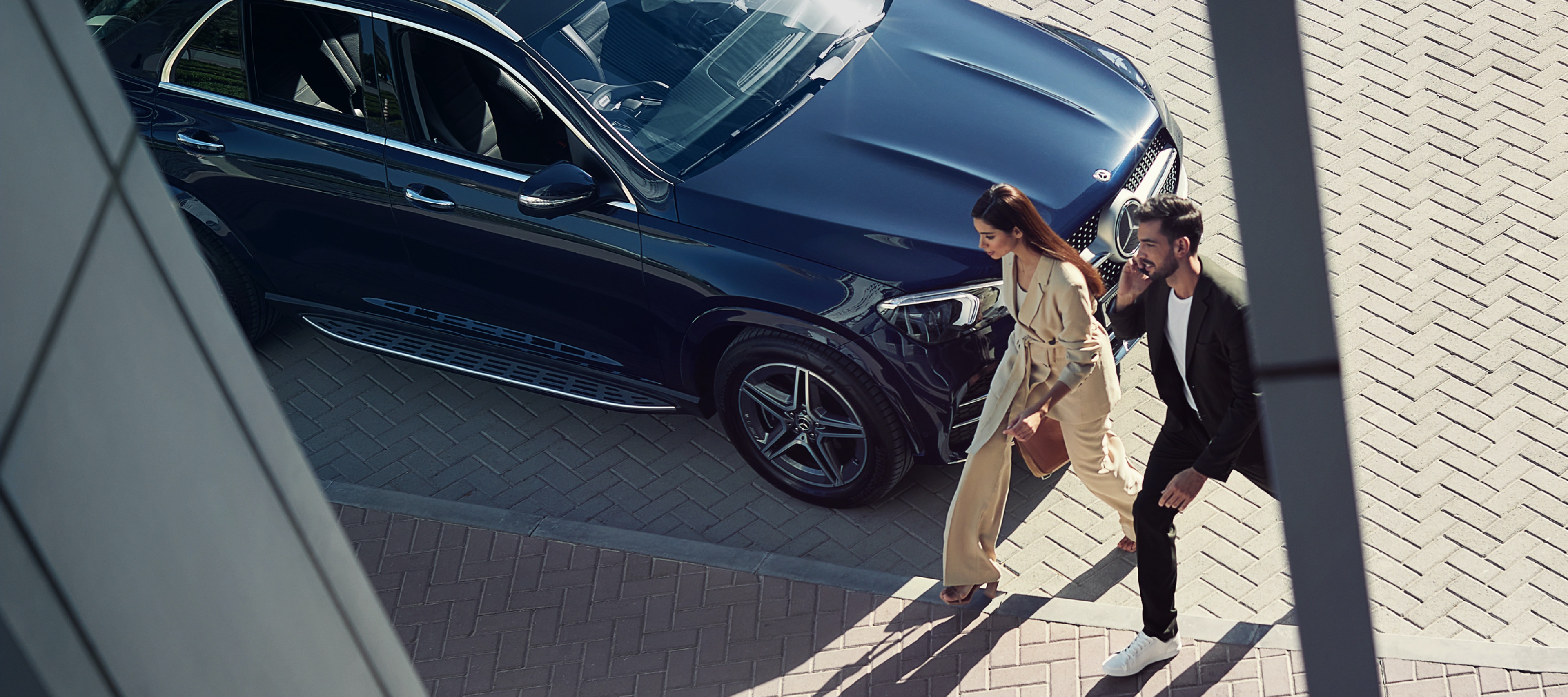 Eine Frau und ein Mann gehen an ihrem Mercedes-Benz vorbei und sind mit dem Smartphone per Digitalem Extra mit dem Fahrzeug verbunden. Eine Frau und ein Mann gehen an ihrem Mercedes-Benz vorbei und sind mit dem Smartphone per Digitalem Extra mit dem Fahrzeug verbunden.